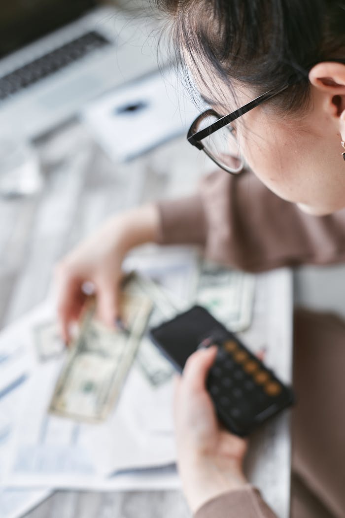 contact-img A woman calculates finances using a calculator with banknotes and documents on the table.