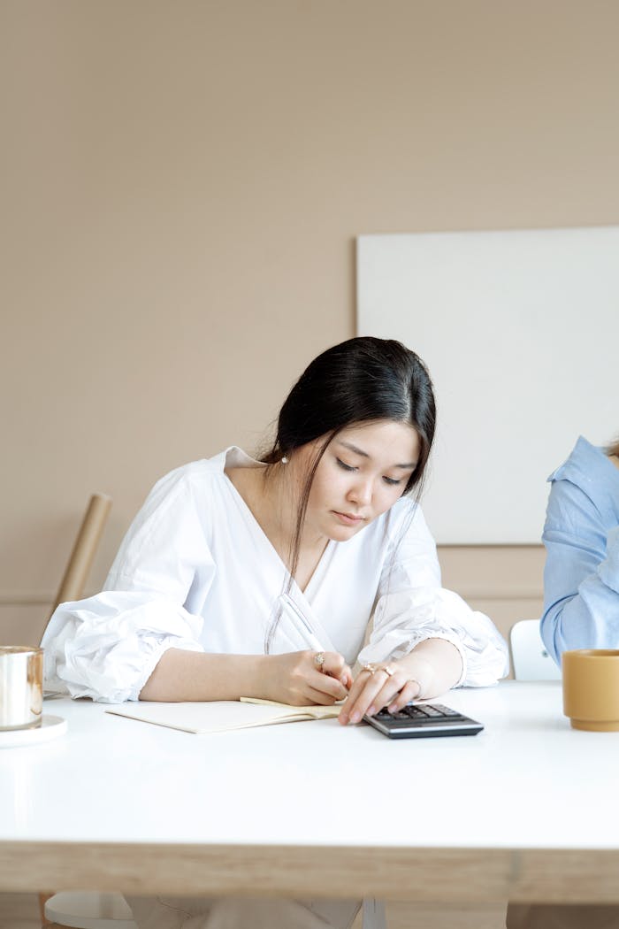 An adult woman attentively doing calculations on a calculator at a desk in a modern office setting.
